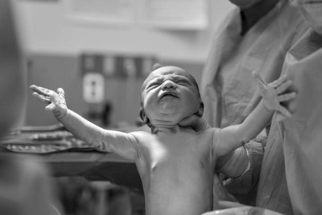 Nyfödd bebis sträcker upp armarna. 