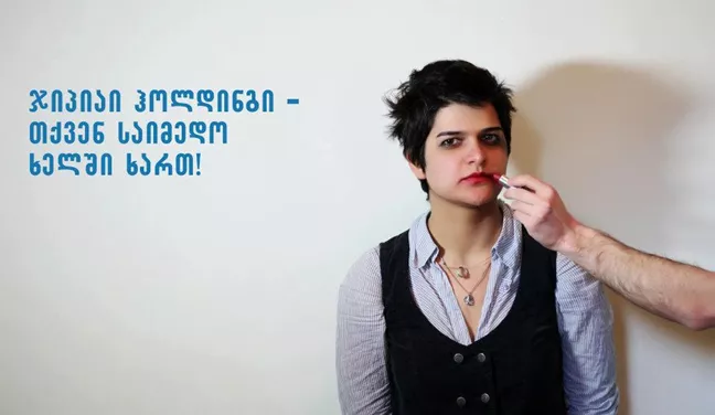 En person i mörk, kortklippt frisyr blir sminkad. 