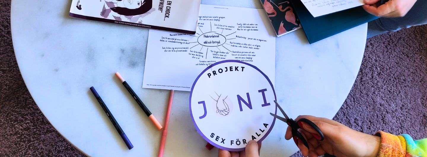 Händer klipper och pysslar vid ett bord med material från RFSU Malmös projekt Joni.  