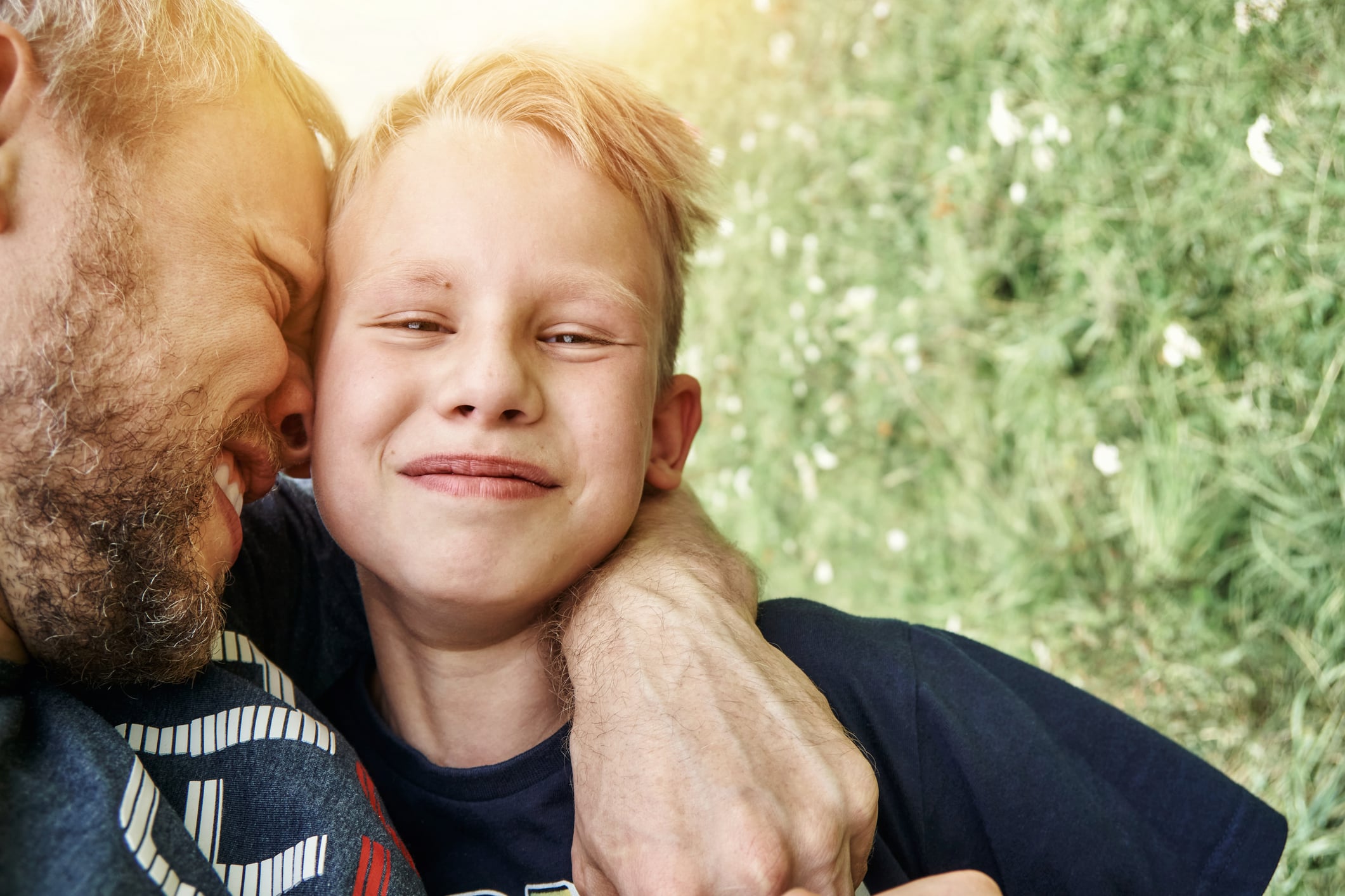 En pappa håller om och har sitt ansikte mot sin sons kind. Sonen ler och tittar in i kameran.