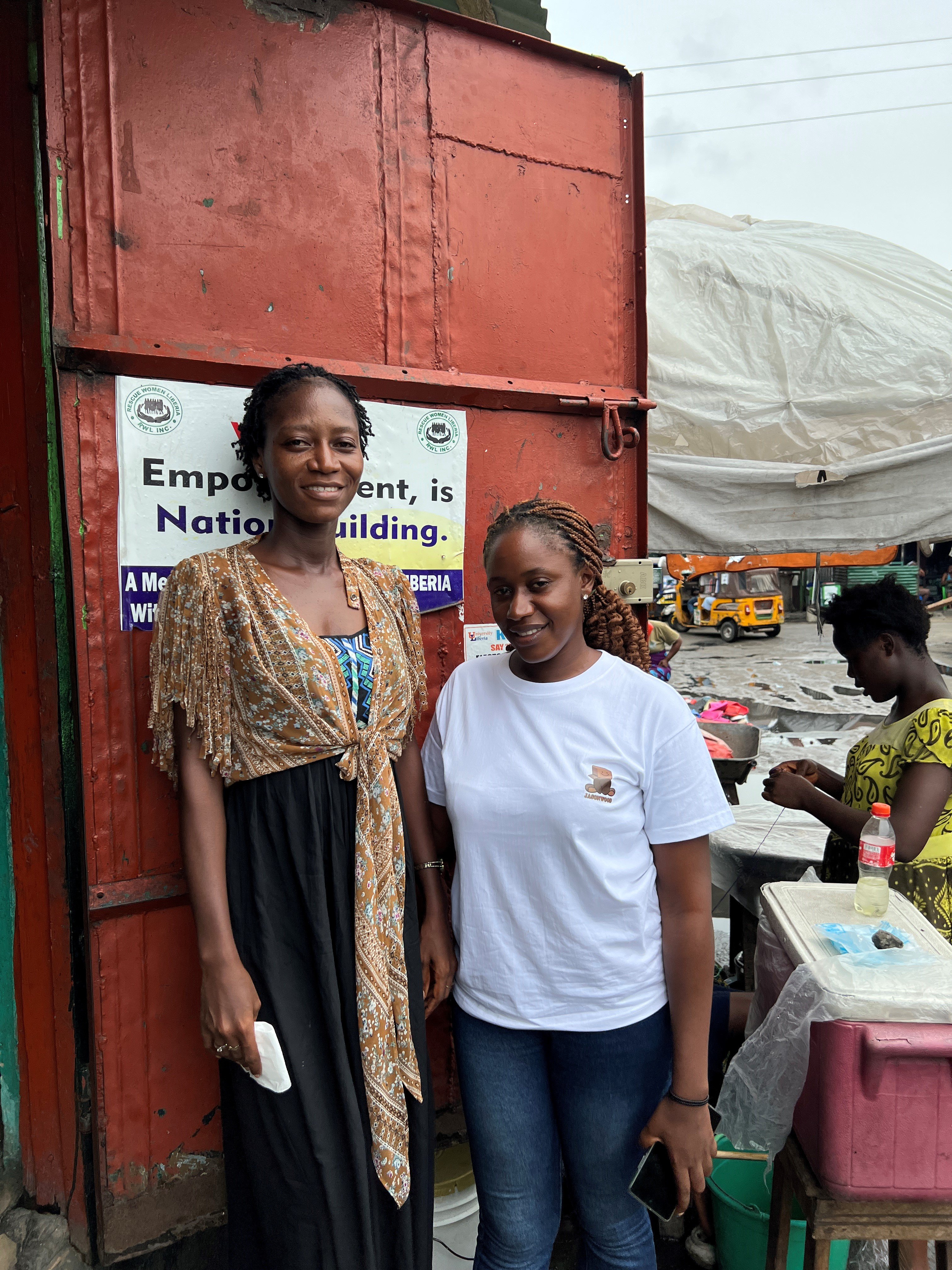 Two women are standing in front of an orange container and smiling to the camera.