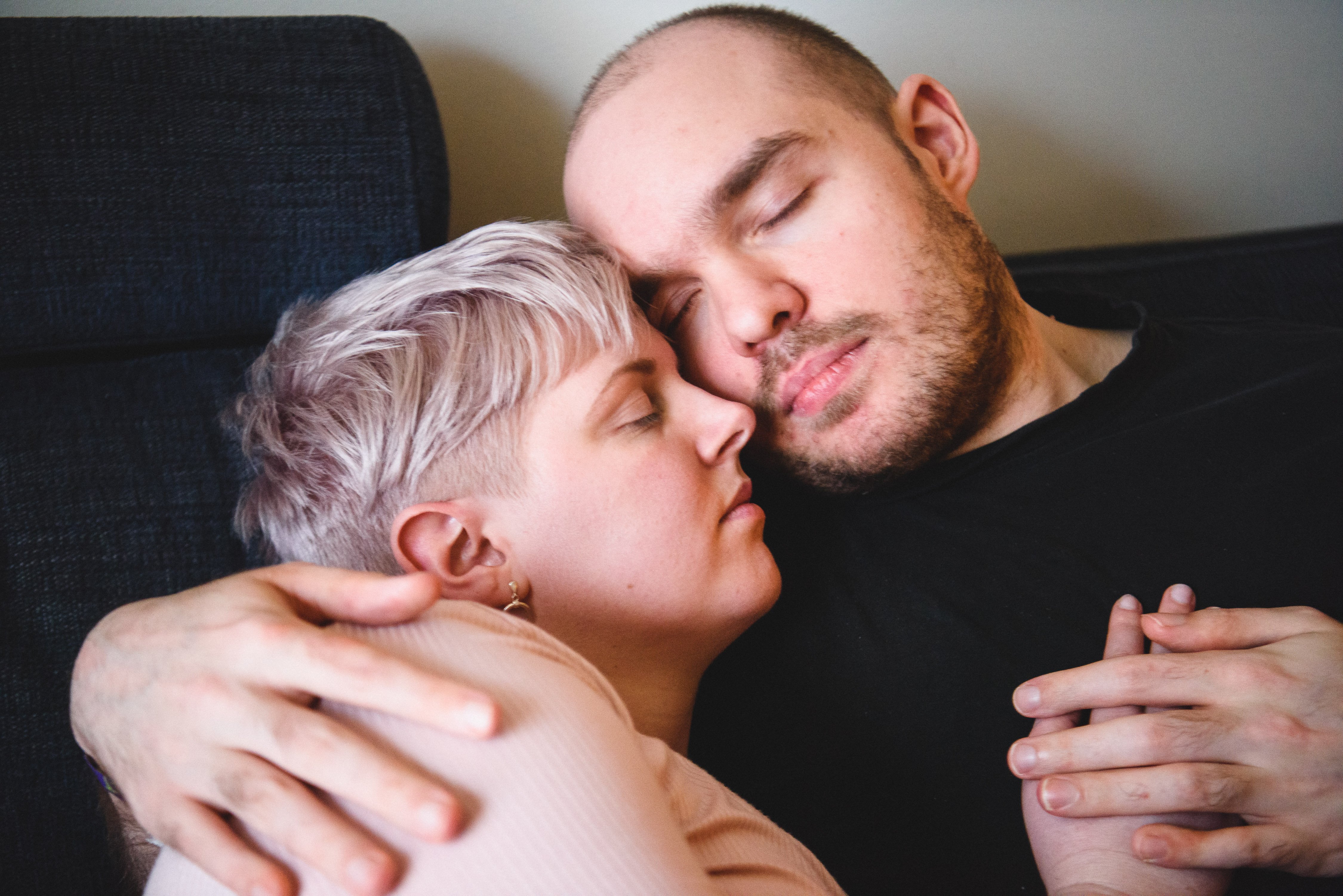 Två personer sitter på en soffa och kramas, blundar och håller handen.