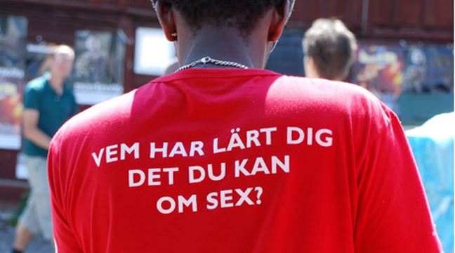 En person bakifrån med en röd t-shirt och vit text på ryggen: VEM HAR LÄRT DIG DET DU KAN OM SEX?
