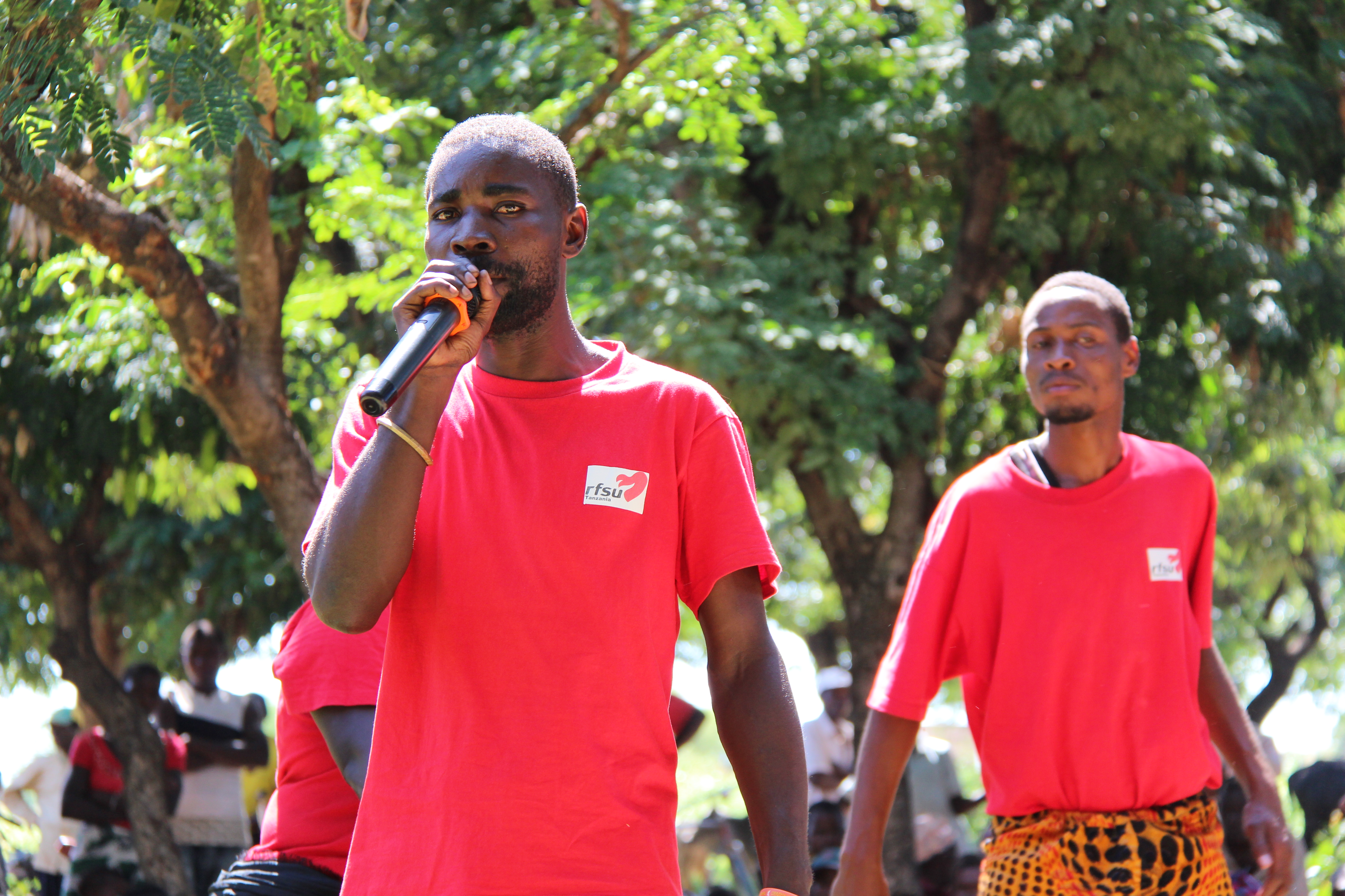 Two people with red rfsu-shirts outdoors. One is speaking into a microphone.