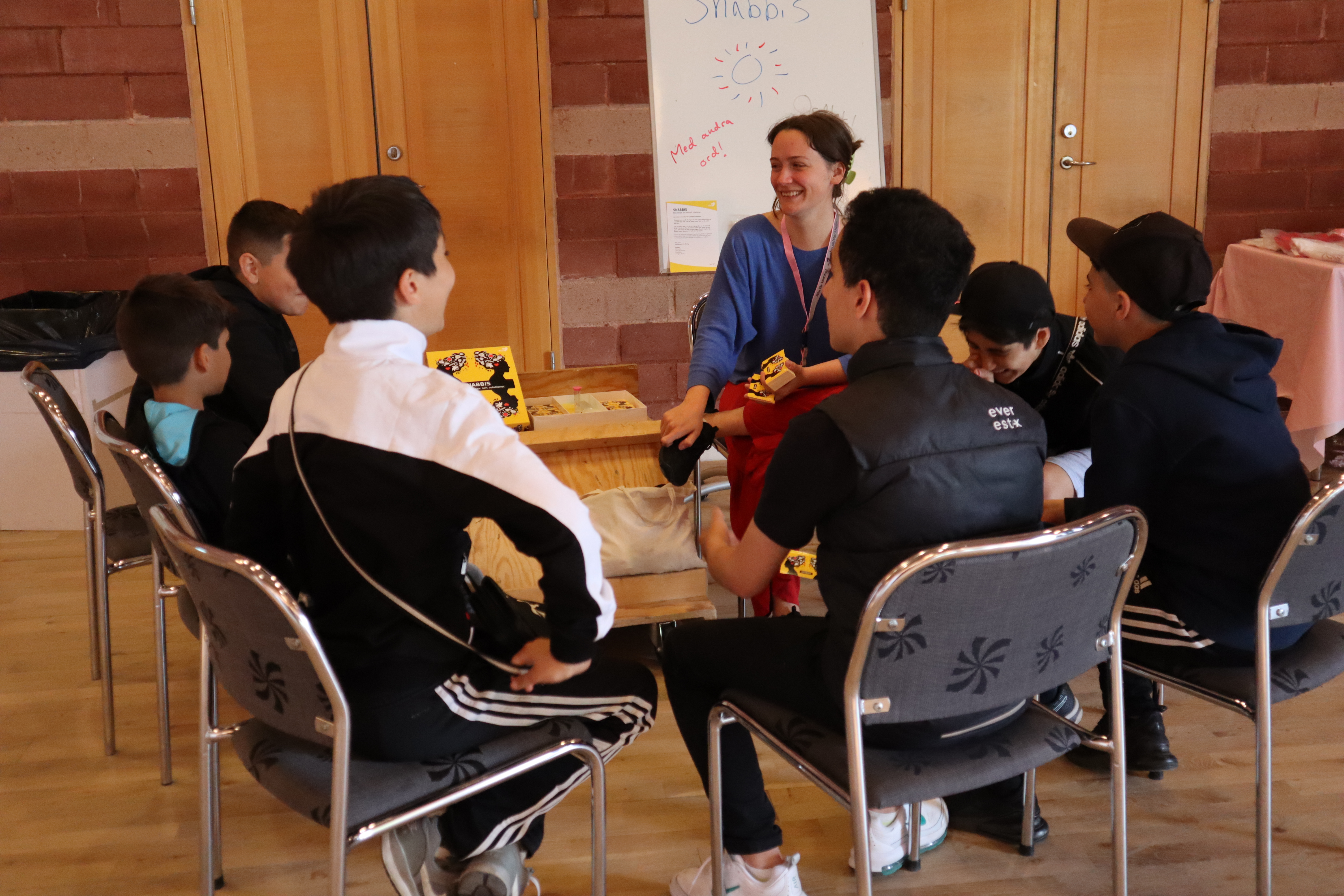 En grupp ungdomar och en pedagog sitter på stolar i en ring och ser ut att spela ett spel