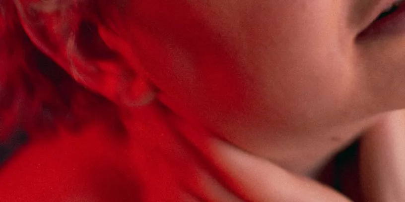 En kvinna med kort rosa hår syns i profil. Hon blundar och smeker sin hals.  