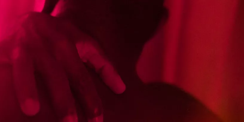 En man bakifrån för sin hand ovanför sin axel och ned mot ryggen. Rummet är fyllt av varmt rött ljus. 