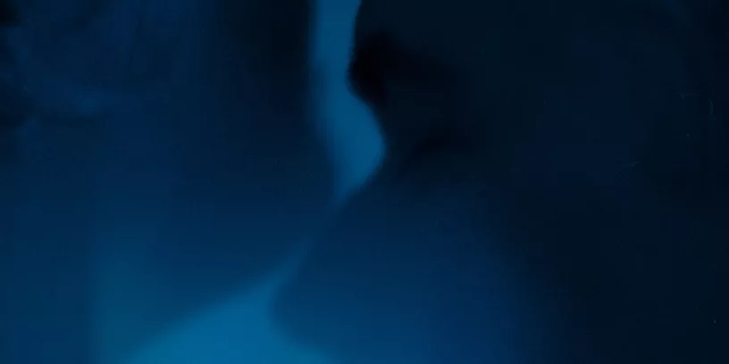 Två ansikten vänd mot varandra i profil. Det är blått ljus i rummet. 